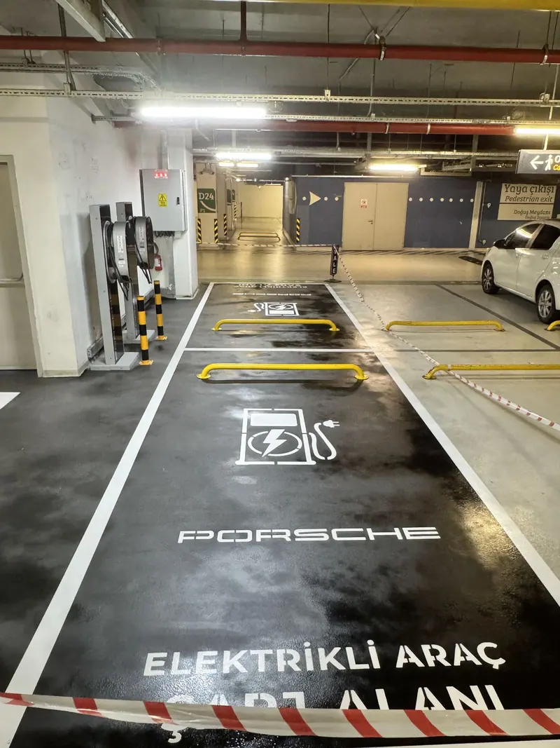 Kapalı otoparkta koyu zemin üzerine beyaz yazılı elektrikli araç şarj alanı
